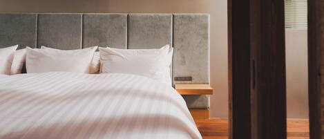 Uma cama bem arrumada com roupa de cama branca, cabeceira estofada cinza e mesa de cabeceira de madeira com gaveta.