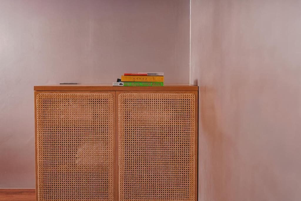 Un mueble de madera con panel frontal tejido y una pila de libros encima.