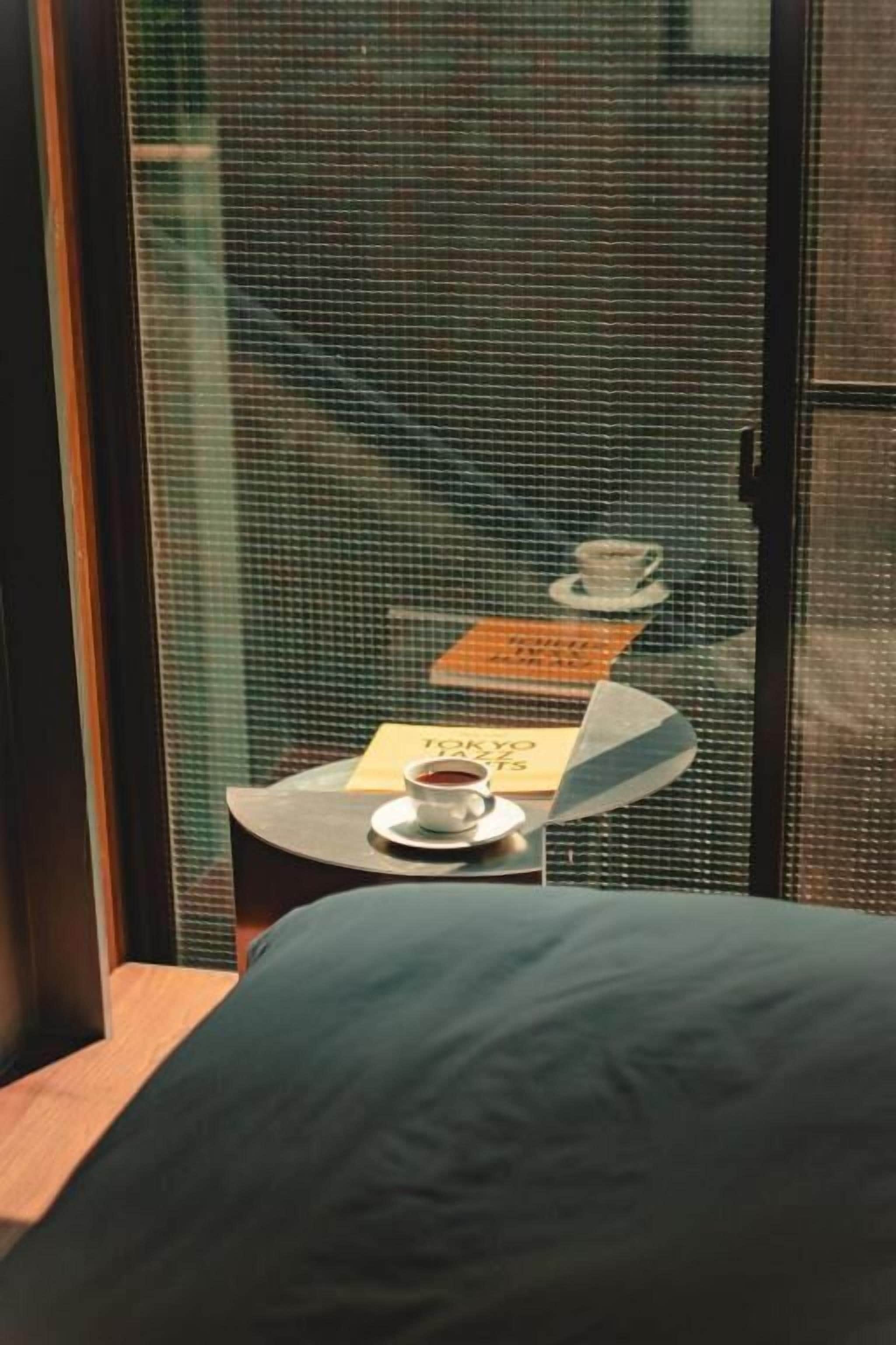 Une chambre d’hôtel avec un lit, une petite table sur laquelle se trouve une tasse de café, et une pancarte sur laquelle est écrit le mot « Tokyo ».