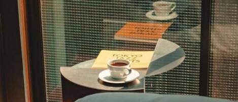 Une chambre d’hôtel avec un lit, une petite table sur laquelle se trouve une tasse de café, et une pancarte sur laquelle est écrit le mot « Tokyo ».