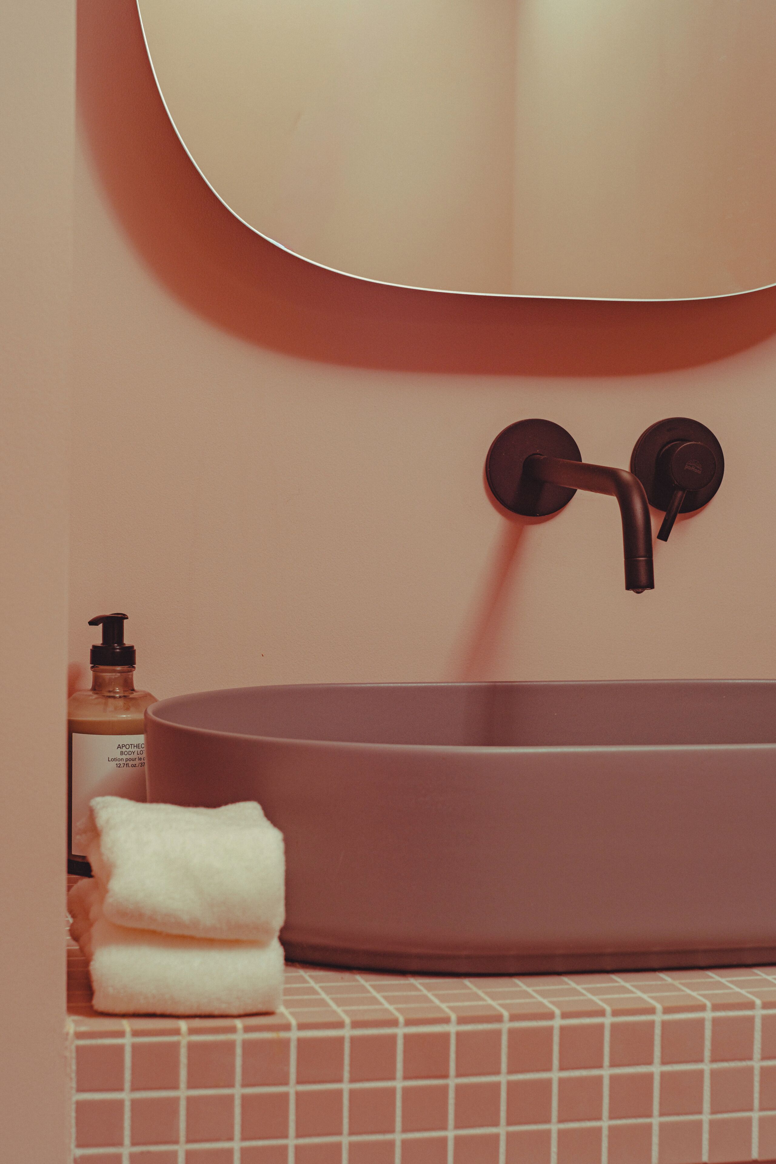 A bathroom with a round sink, a towel, and a bottle of lotion.
