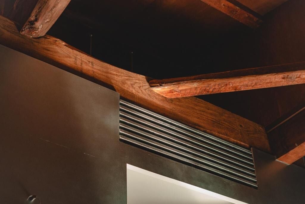 Decke mit freiliegenden Holzbalken und einem Lüftungsgitter.