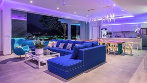 Uma sala de estar moderna com um sofá azul, uma mesa de centro de vidro e uma área de jantar com uma mesa e cadeiras de madeira.