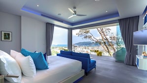 Quarto moderno com uma cama grande, um sofá azul, vista da cidade e um ventilador de teto.