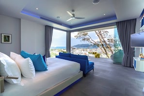 A modern bedroom with a large bed, a blue sofa, a view of the city, and a ceiling fan. - Villa Enjoy - Modern Luxury  in Patong (Tambon Patong)