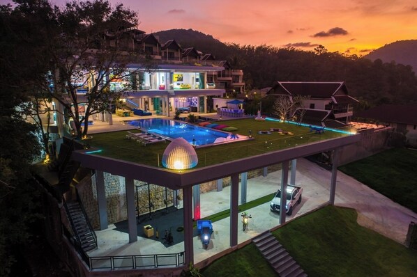 A modern villa with a swimming pool, outdoor seating, and a glass-enclosed terrace. - Villa Enjoy - Modern Luxury  in Patong (Tambon Patong)
