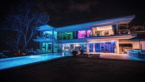 Uma casa moderna de vários andares com piscina, área de estar externa e fachada bem iluminada.