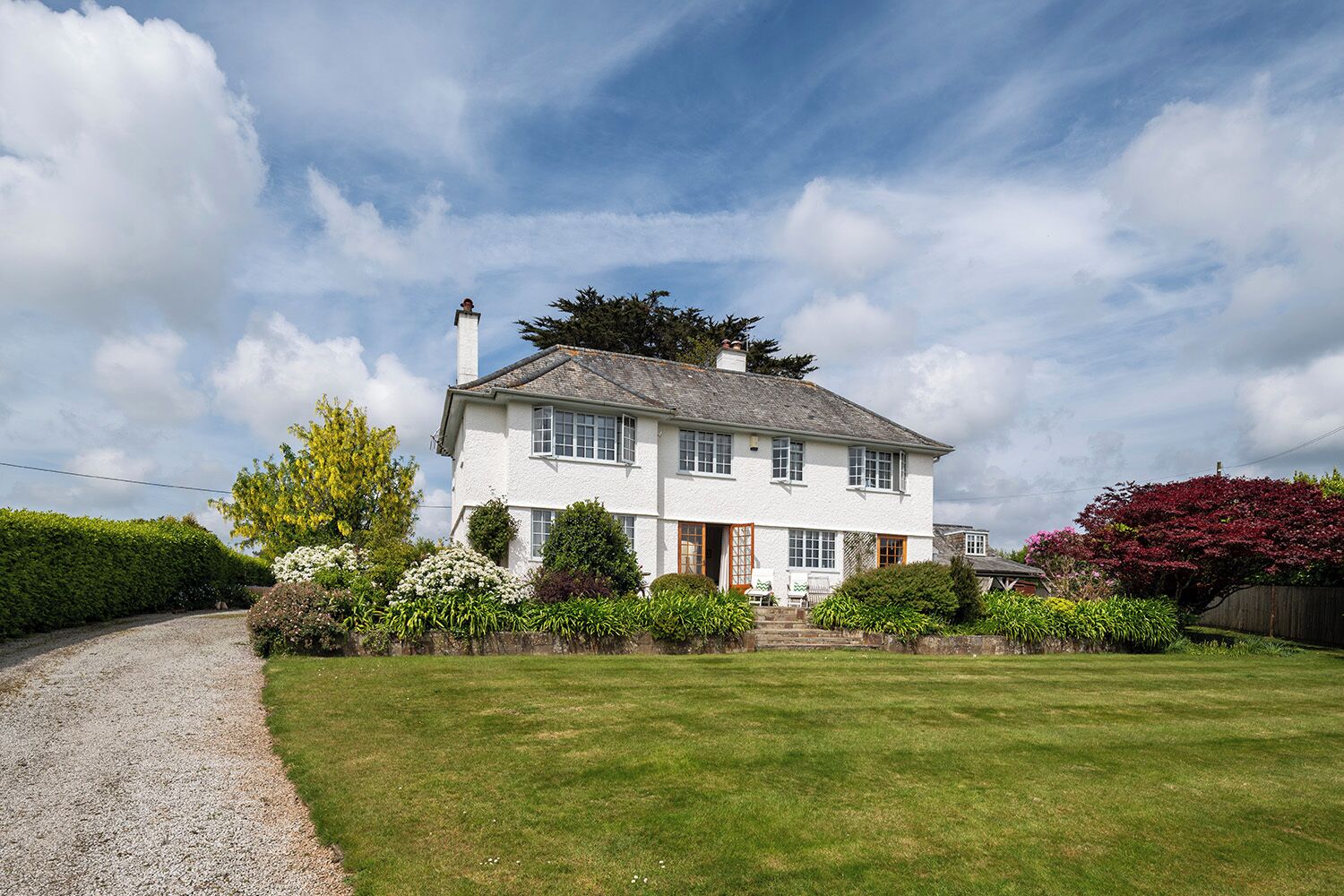 A two-story house with a gravel driveway and a well-maintained lawn.