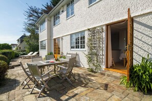 Eine Terrasse mit Tisch und Stühlen, eine Holztür und ein weißes Gebäude mit Fenstern.