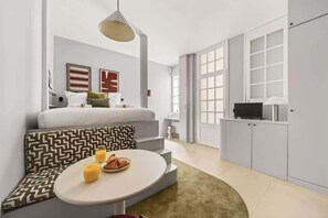 Una habitación moderna con sofá, una mesa de comedor con desayuno, televisor y un amplio ventanal.