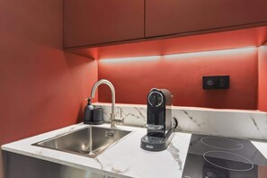 Una cocina compacta con un lavamanos de acero inoxidable, una cafetera y una cocina de inducción.