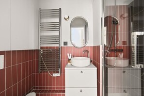 Un baño con tocador blanco, un espejo redondo, toallero y zona de ducha.