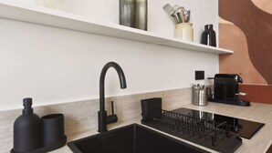 A modern kitchen with a black sink, a stainless steel kettle, and a coffee maker on the counter. - A stunning retreat renovated by an architect - Marais (Paris)