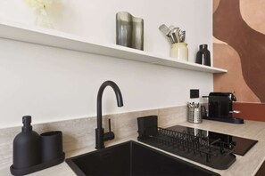 Una cocina moderna con un lavamanos negro, un hervidor de acero inoxidable y una cafetera en la encimera.