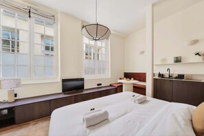 Una habitación de hotel con cama, televisión, escritorio, ventana y kitchenette.