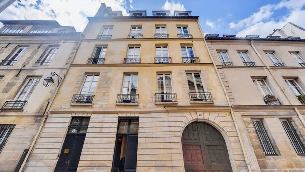 A multi-story building with a classic architectural style, featuring a central entrance with a large arched doorway, multiple windows, and balconies. - A stunning retreat renovated by an architect - Marais (Paris)