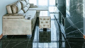 A modern living room with a sectional sofa, a tufted ottoman, a large window with curtains, and a black marble wall.