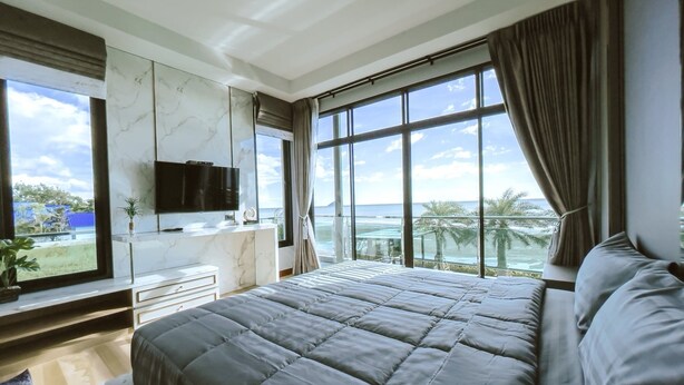 A modern bedroom with a large bed, a TV, and a view of the ocean.