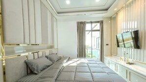A bedroom with a large bed, a TV mounted on the wall, and a view of the outdoors through a window.