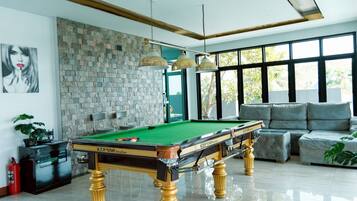 A pool table in a well-lit room with a stone wall, a sofa, and a large window.