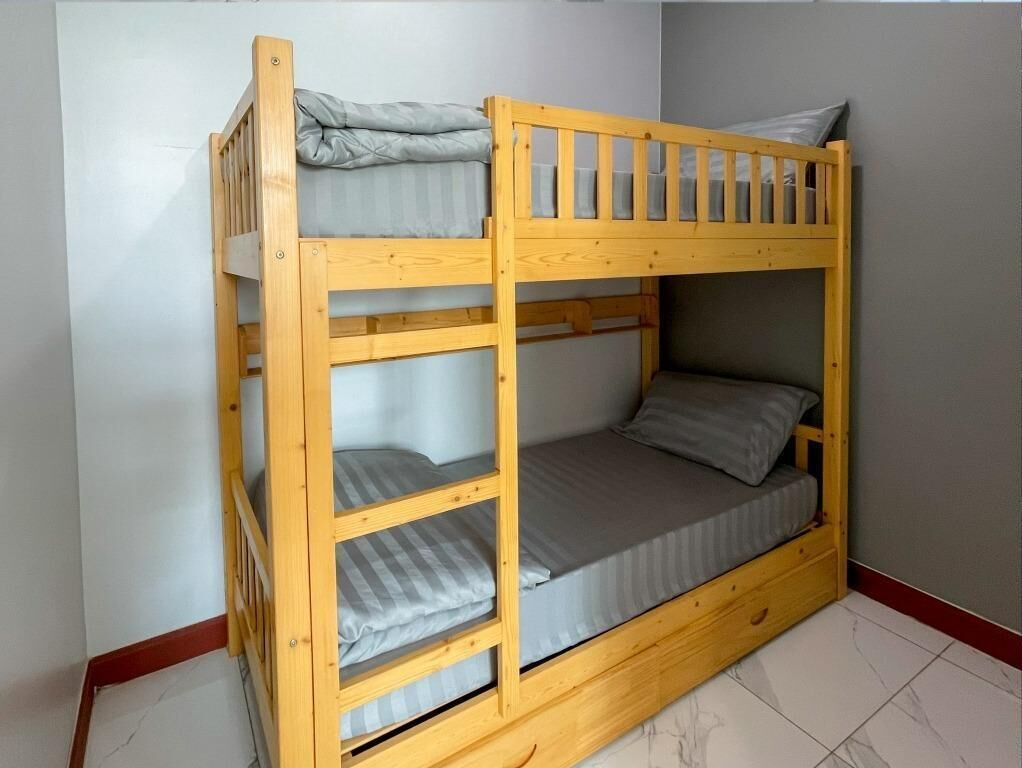 A bunk bed with three levels, grey bedding, and a wooden frame.