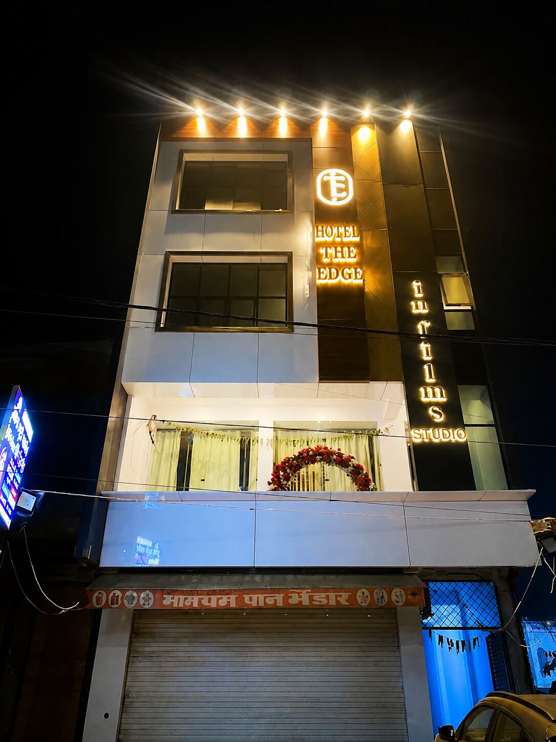 Un hotel con fachada moderna, señalización iluminada y escaparate visible con persiana cerrada.