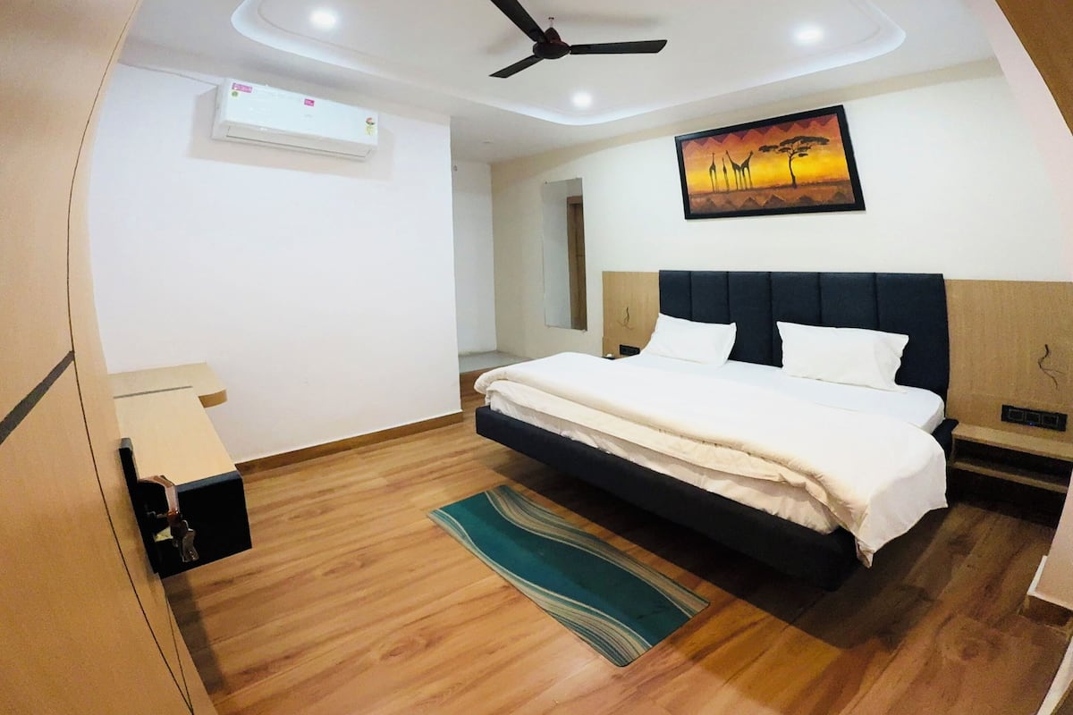 Un dormitorio moderno con cama, ventilador de techo, iluminación empotrada y un cuadro en la pared.