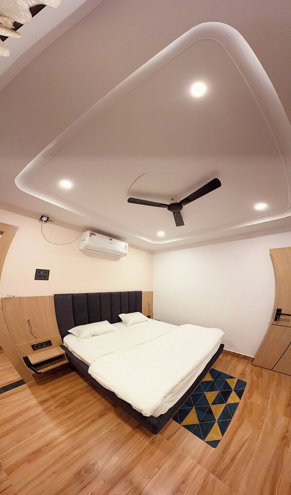A modern bedroom with a bed, ceiling fan, recessed lighting, and an air conditioning unit.
