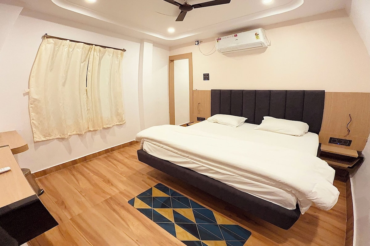 Una habitación de hotel moderna con una cama grande, suelo de madera, ventilador de techo y aire acondicionado.