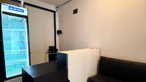 A reception area with a black reception desk, a white table with a white tablecloth, a black leather couch, and a blue star refrigerator. - Hotel The Edge (Huzur)
