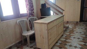 A room with a wooden cabinet, two plastic chairs, a patterned floor, and a staircase. - Kaas Home Stay (Chitkul)