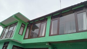 A multi-story building with large windows and a green facade. - Kaas Home Stay (Chitkul)