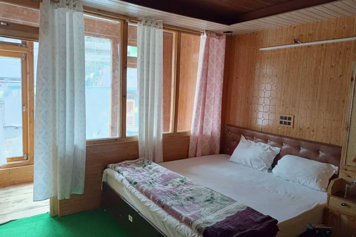 A bedroom with a bed, curtains, a wooden headboard, a green carpet, and a window with a view.