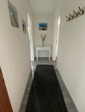 A hallway with a black carpet, white walls, and a small white console table with a vase of dried pampas grass.