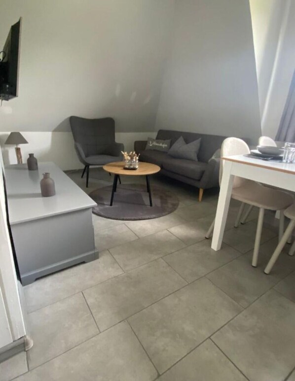 A compact living space with a sofa, a coffee table, a dining table, and a TV mounted on the wall.