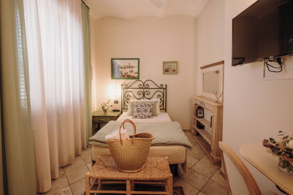 A bedroom with a bed, a television, a fireplace, and a window with curtains.