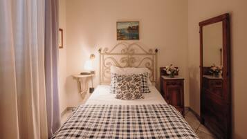 A bedroom with a bed, a nightstand, a dresser, a mirror, a painting on the wall, and a window with curtains.