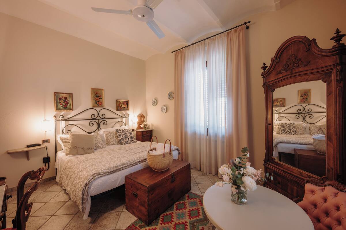 A bedroom with a bed, bedside table, lamp, dresser, mirror, and a round table with a vase.