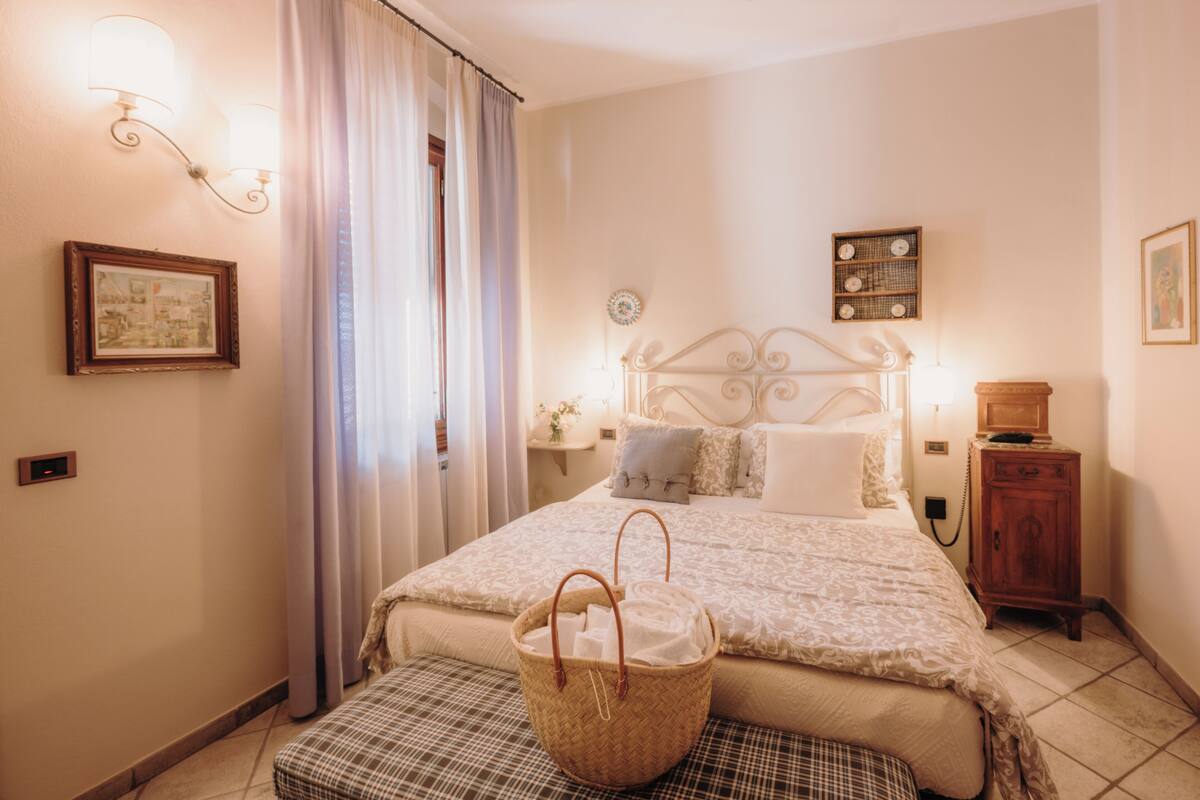 A neatly arranged bedroom with a bed, bedside tables, a lamp, a wall-mounted clock, and a basket.