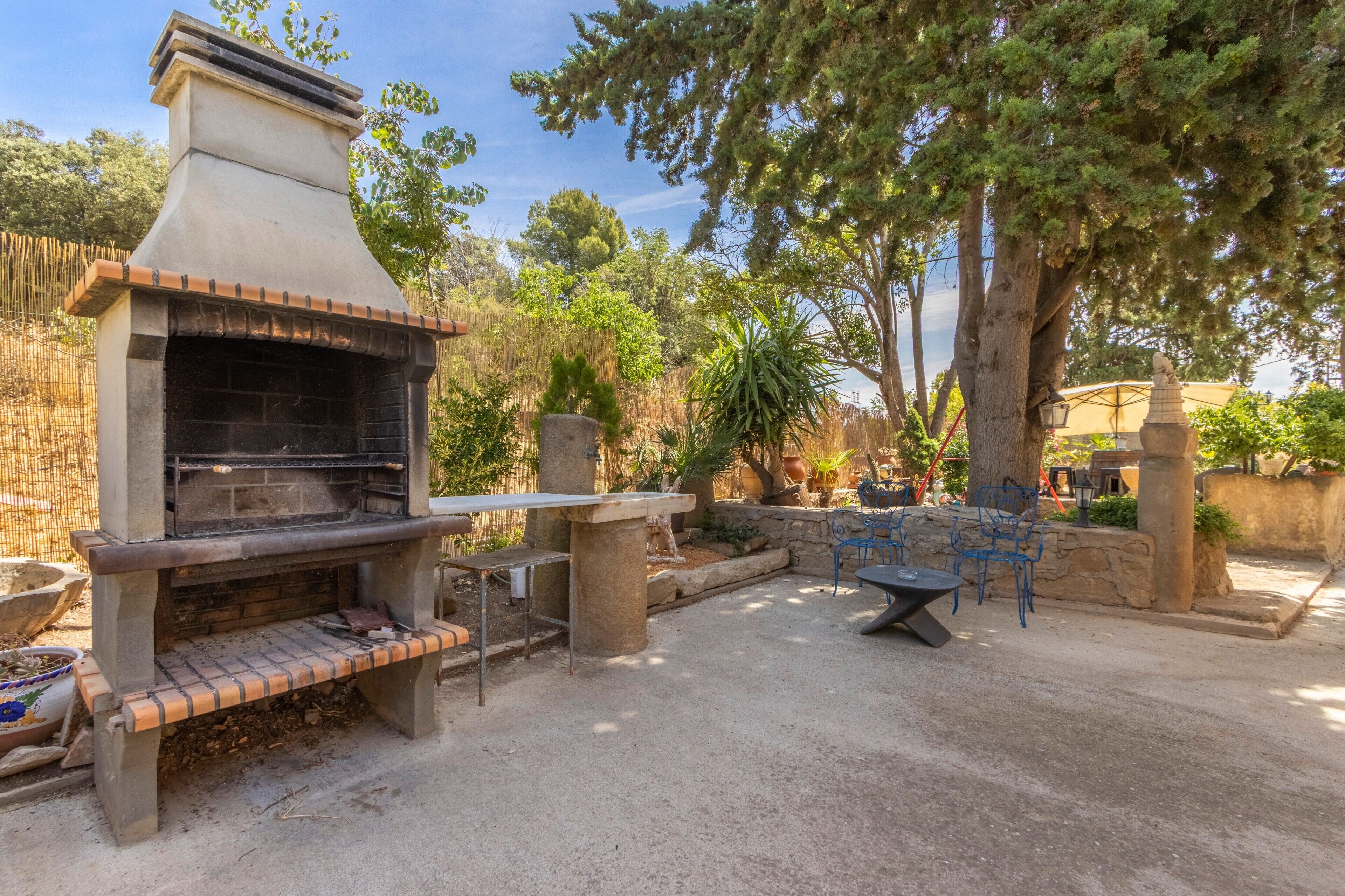 Un patio exterior con una parrilla de piedra, zona de estar y plantas en macetas.