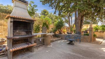 Un patio exterior con una parrilla de piedra, zona de estar y plantas en macetas.