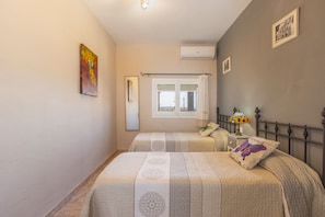 A bedroom with two beds, a window, an air conditioner, and a nightstand with a lamp.