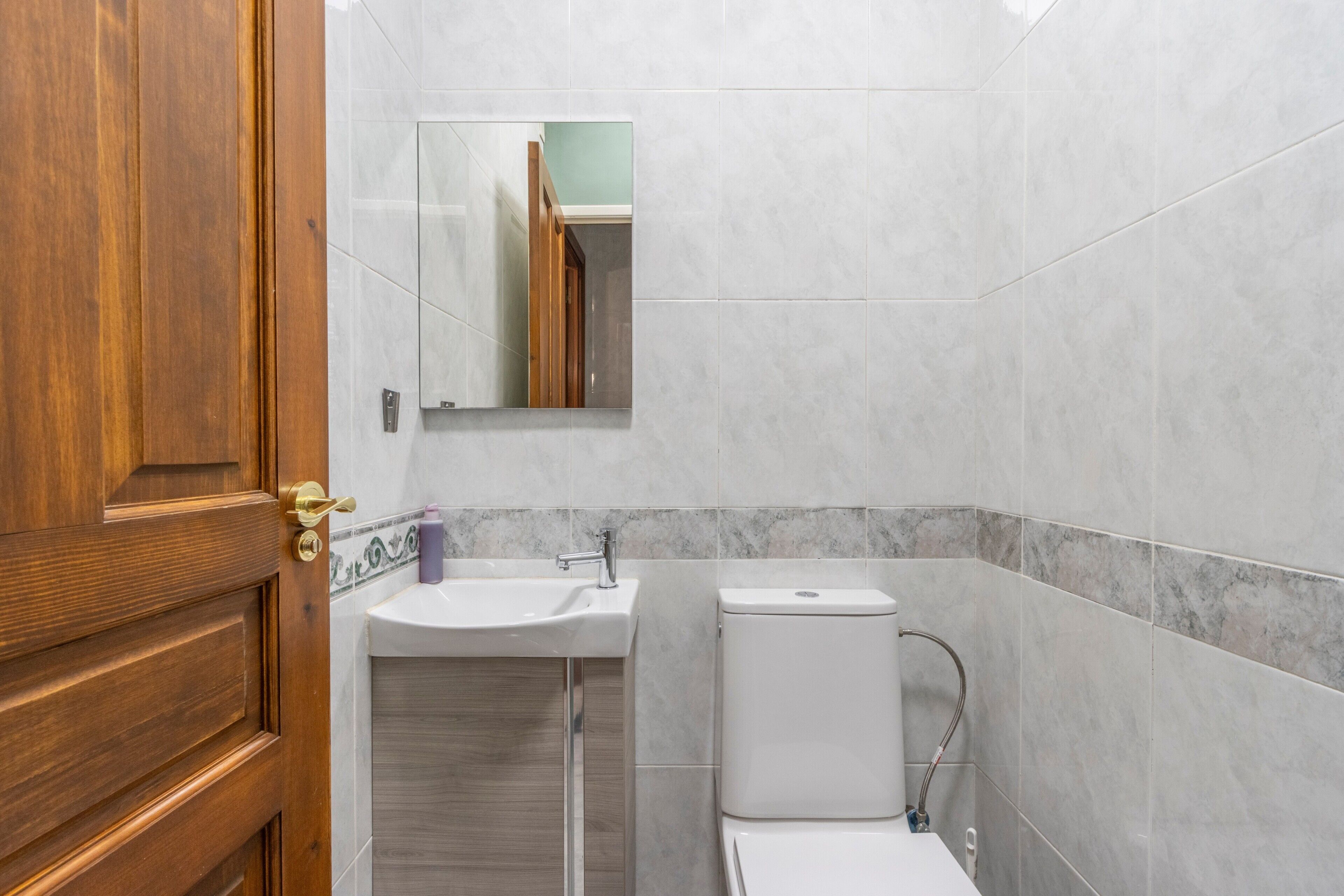 A bathroom with a wooden door, a sink, a mirror, and a toilet.