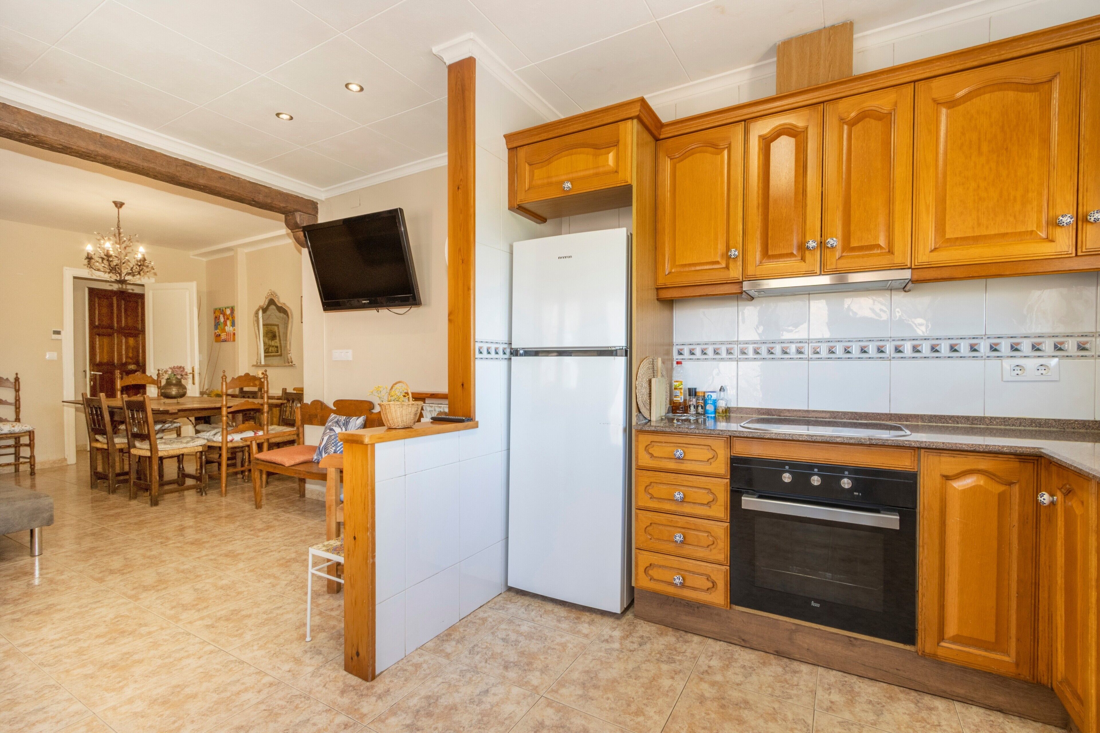 Una cocina con armarios de madera, horno empotrado y televisor sobre la encimera.