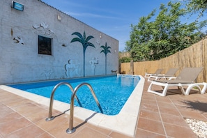A swimming pool with a metal ladder, white lounge chairs, and a mural on the wall.