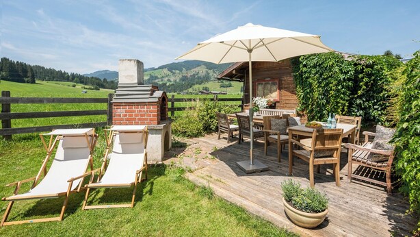 Una terraza de madera con mobiliario exterior, zona de barbacoa y vistas al campo.