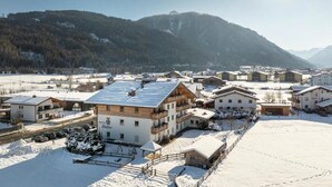 Un pueblo cubierto de nieve con edificios de madera tradicionales, una estación de esquí y montañas al fondo.