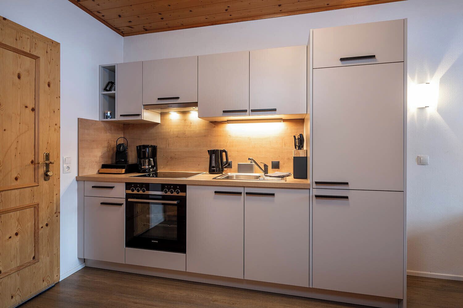 Una cocina moderna con electrodomésticos integrados, techo de madera y diseño de armarios blancos.