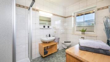Baño con ducha, lavamanos, inodoro y ventana con vistas.