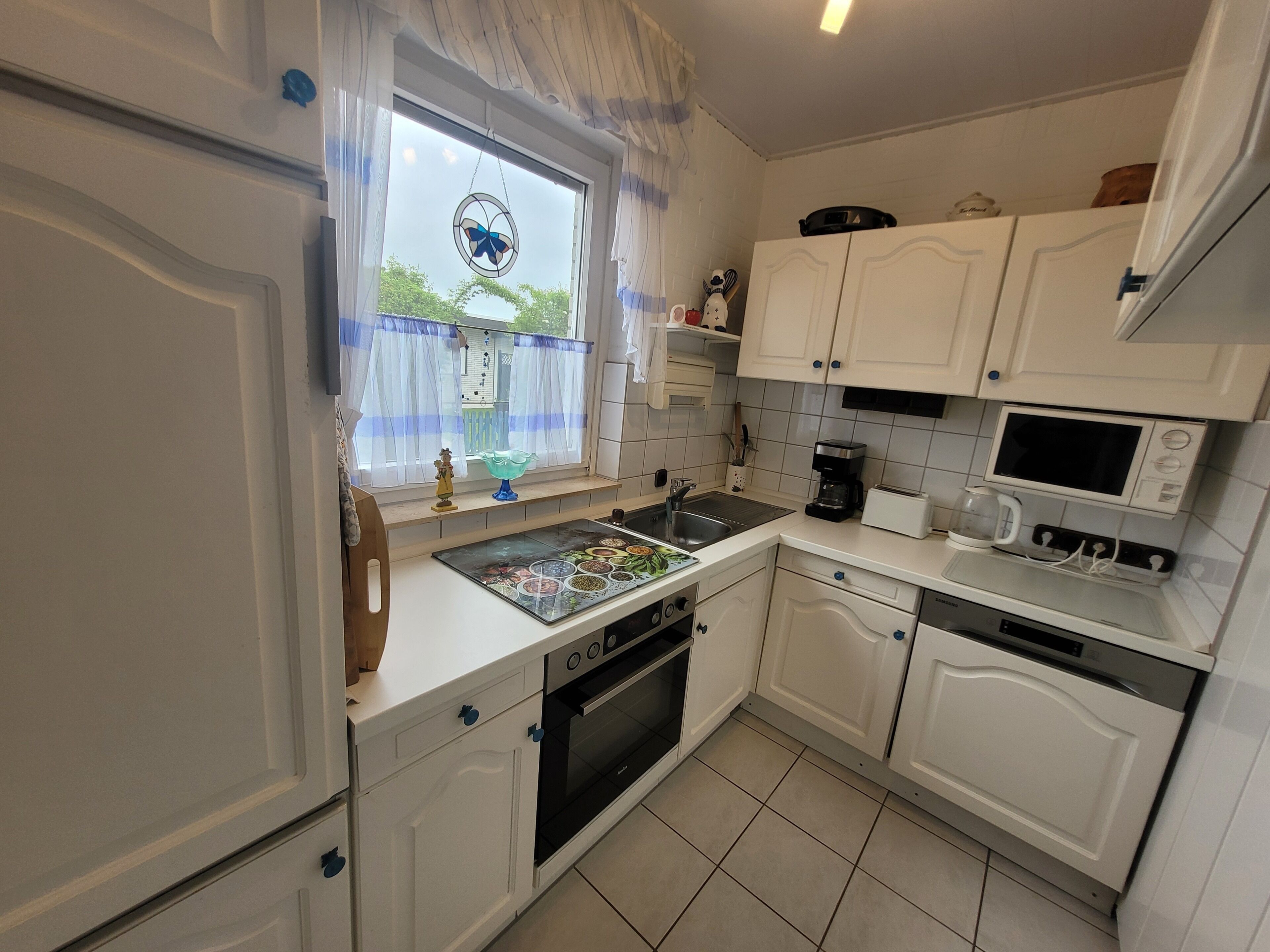 A kitchen with white cabinets, a stove, a microwave, and a window with a blue curtain.